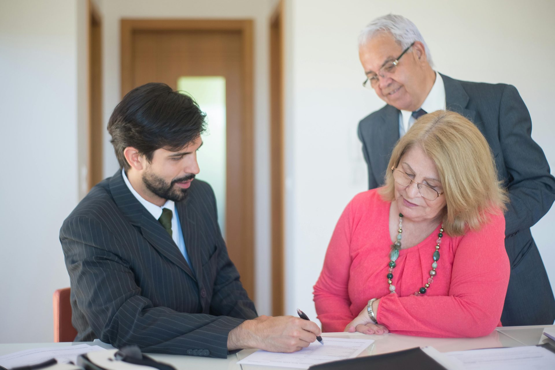 Senior couple signing real estate documents with an agent in a modern office setting.