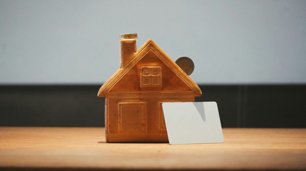 A small house bank with a coin and blank card.